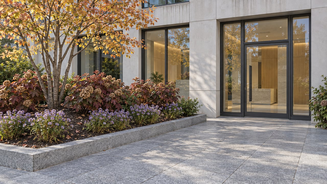 A contemporary apartment entrance beside a raised stone planting bed with golden serviceberry leaves, burgundy oakleaf hydrangeas and lavender asters.