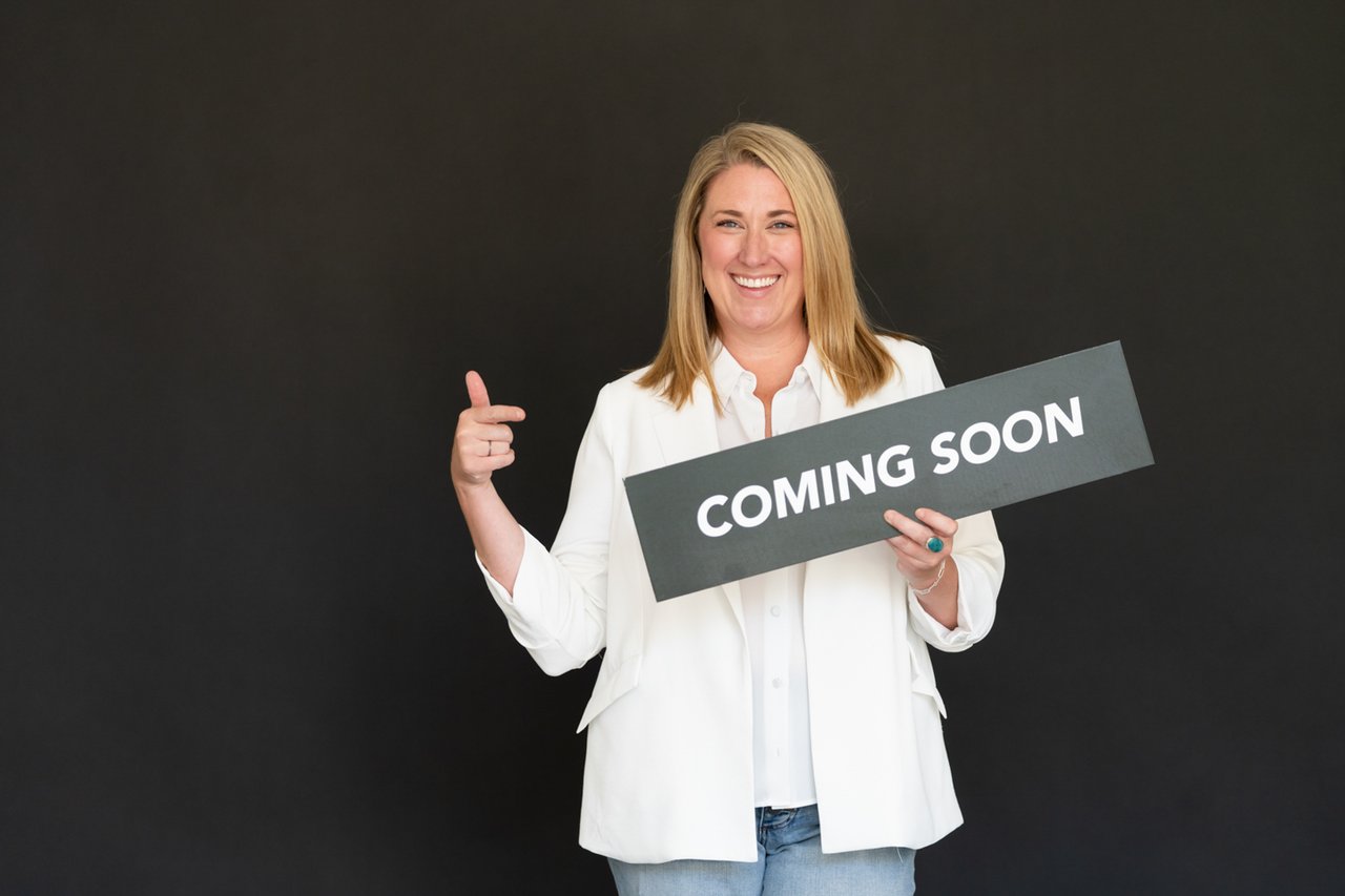 Kathryn Tighe holding a “Coming Soon” sign, Colorado real estate agent helping clients decide whether to sell or buy first