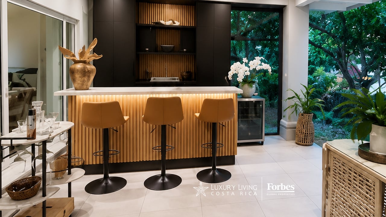 Remodeled kitchen with a warmly lit wood-slat island, three bar stools, and windows overlooking greenery.