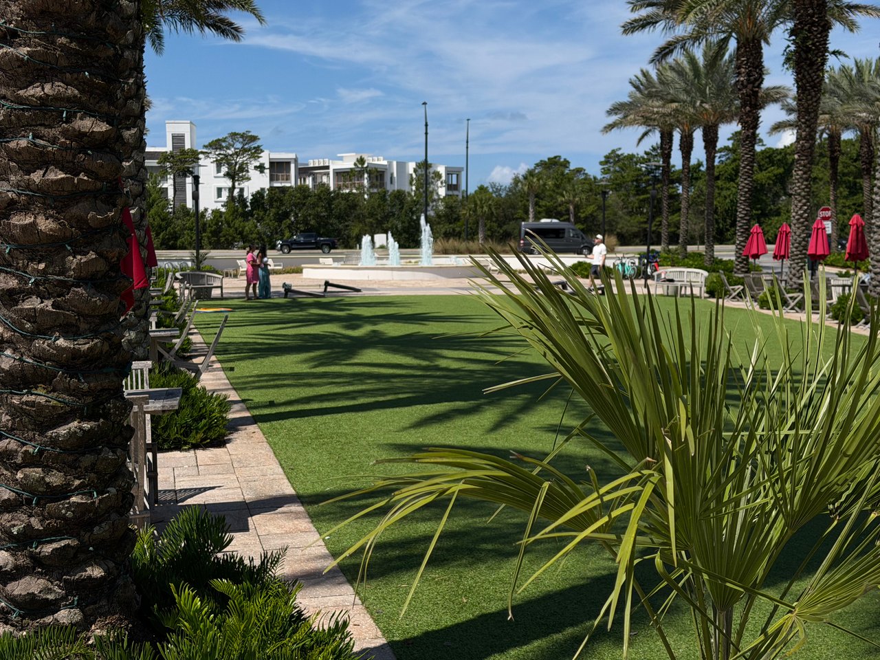 A beautifully manicured green lawn and central water fountain surrounded by palm trees in Alys Beach.