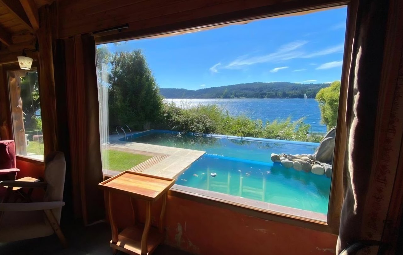 Interior seating area with lake and swimming pool views through a large window.
