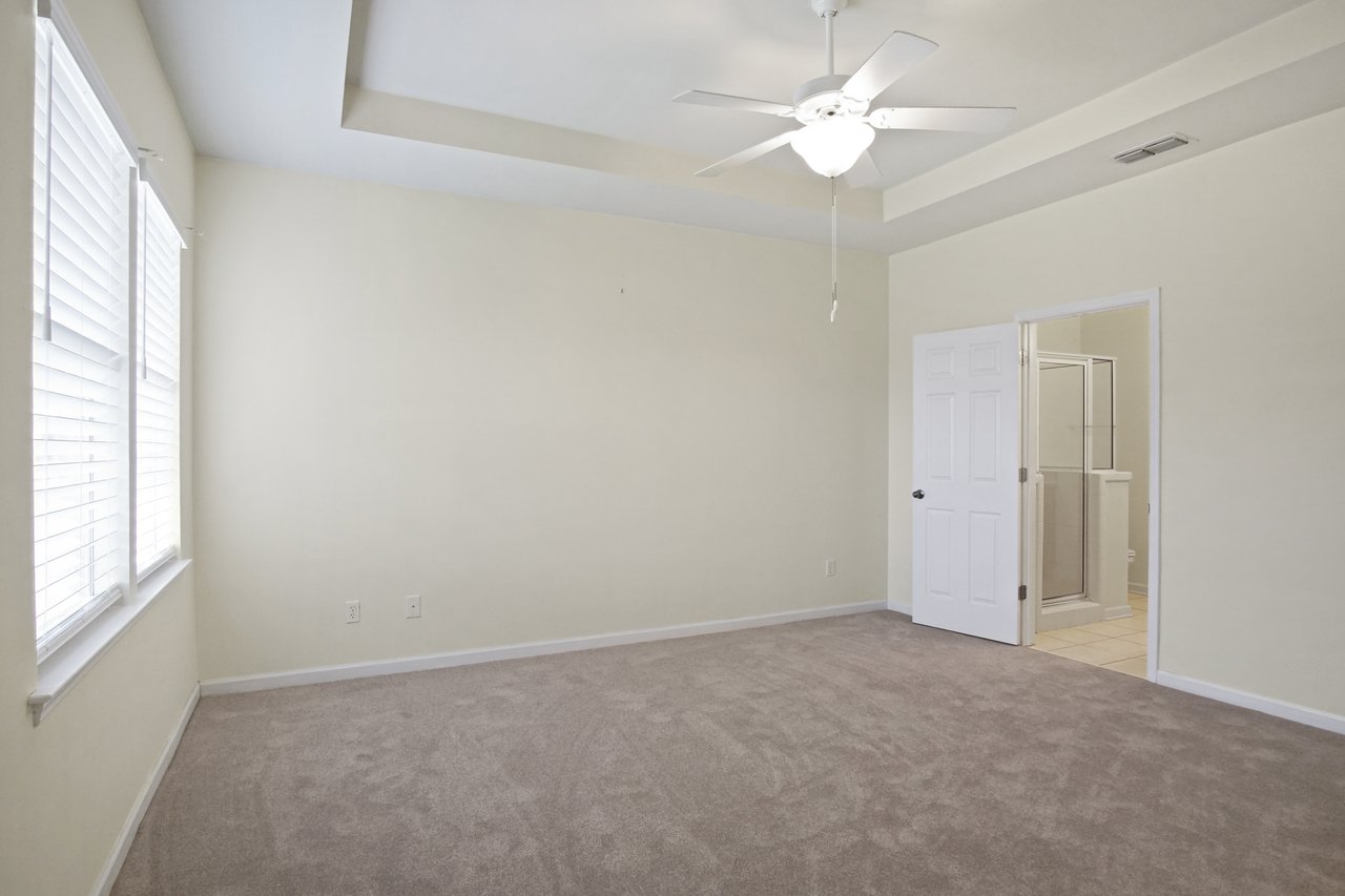Primary bedroom at 5441 Hampton Hill Circle, Tallahassee, Florida 32311 with tray ceiling, ceiling fan, and doorway to ensuite bathroom.