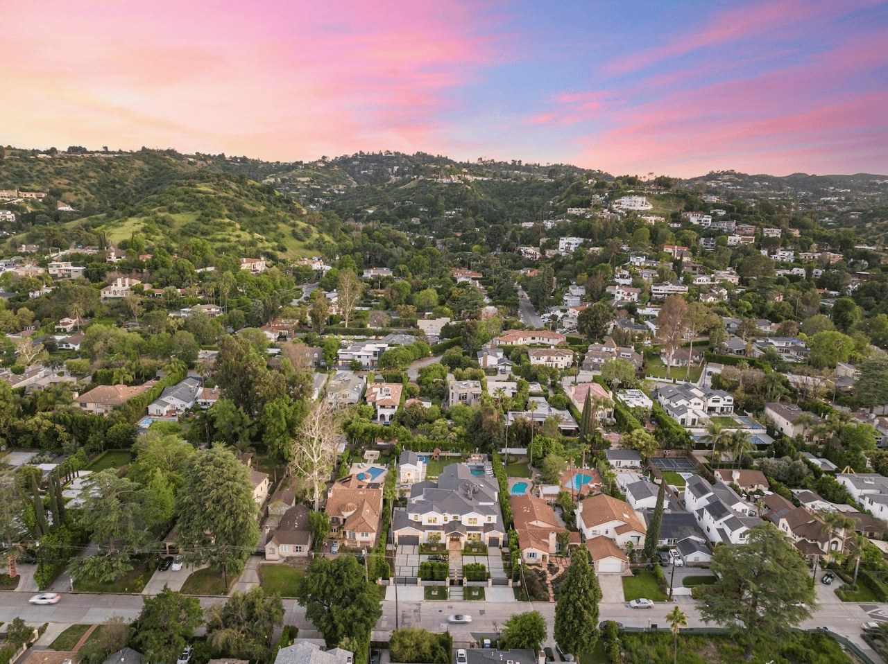 Aerial view of hillside homes and pools beneath a pink sunset sky