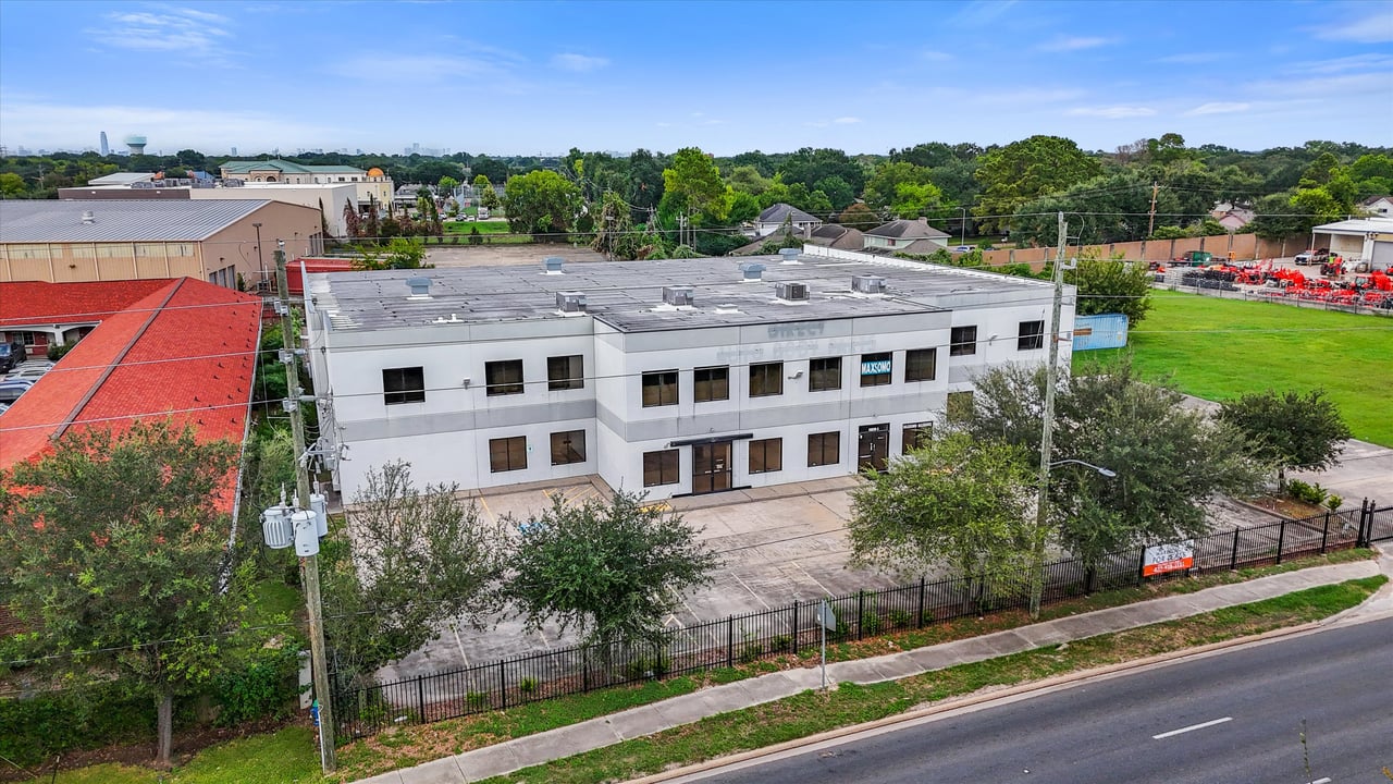 Aerial view of a two-story commercial building with a paved forecourt and fenced frontage.