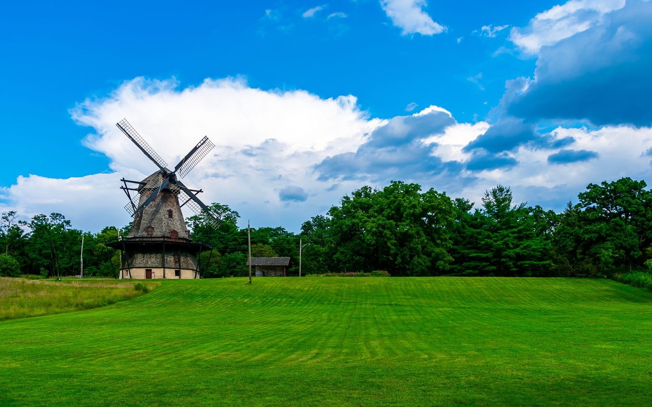 Historic windmill on a broad green lawn in Batavia, beneath a bright blue sky.