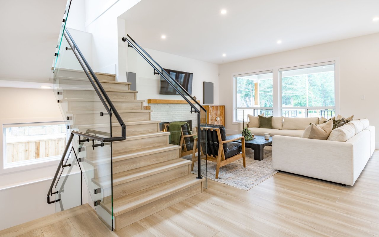 Living room with a glass-railed staircase, white sectional sofa, and large windows.