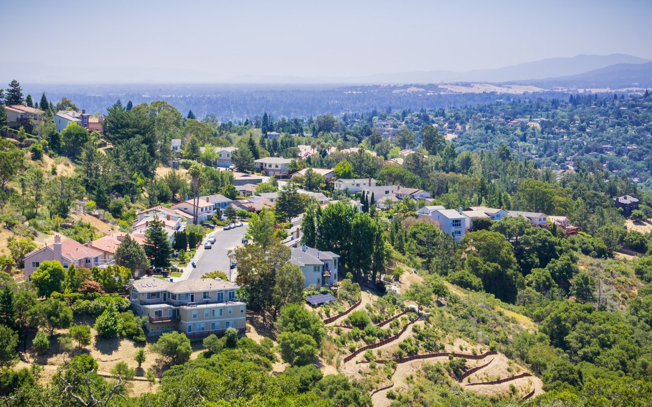 Hillside neighborhood with scattered homes, a winding street, and a distant valley view.