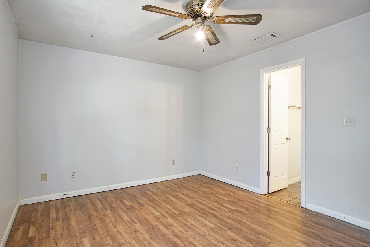 An empty room featuring hardwood floors and a ceiling fan, creating a spacious and airy atmosphere.