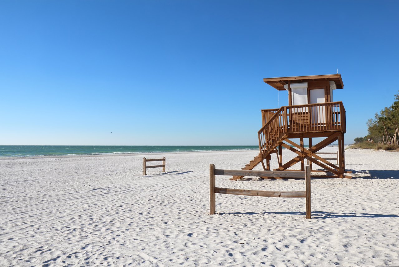 White-sand beach with a wooden lifeguard tower beside blue-green Gulf water.