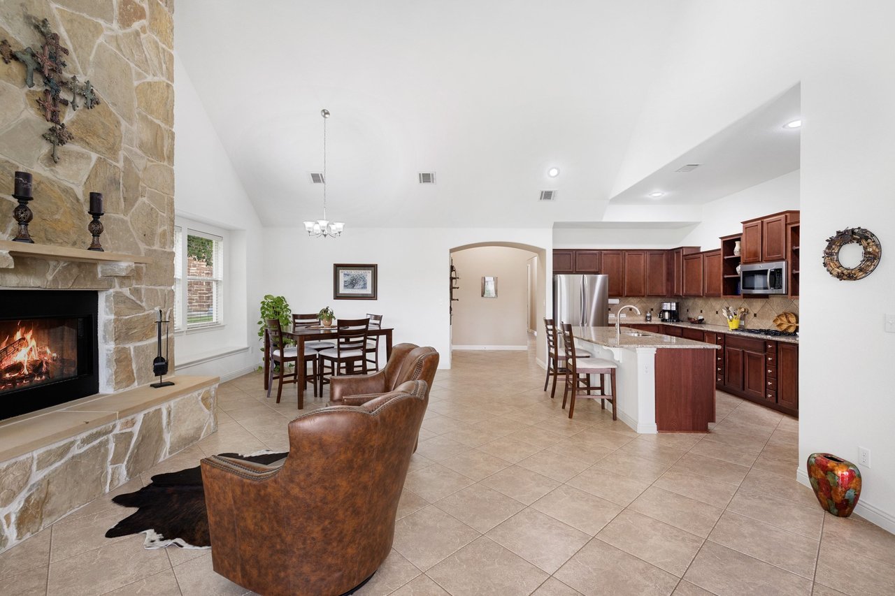Open-plan living and kitchen area with a stone fireplace, vaulted ceiling, and dark wood cabinetry.