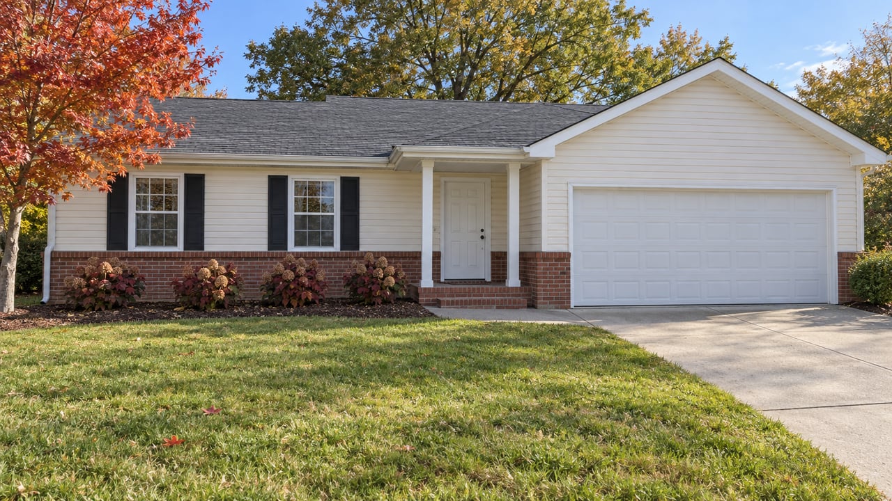 Cream-sided ranch with brick accents, an attached two-car garage and a broad autumn lawn beneath mature trees.