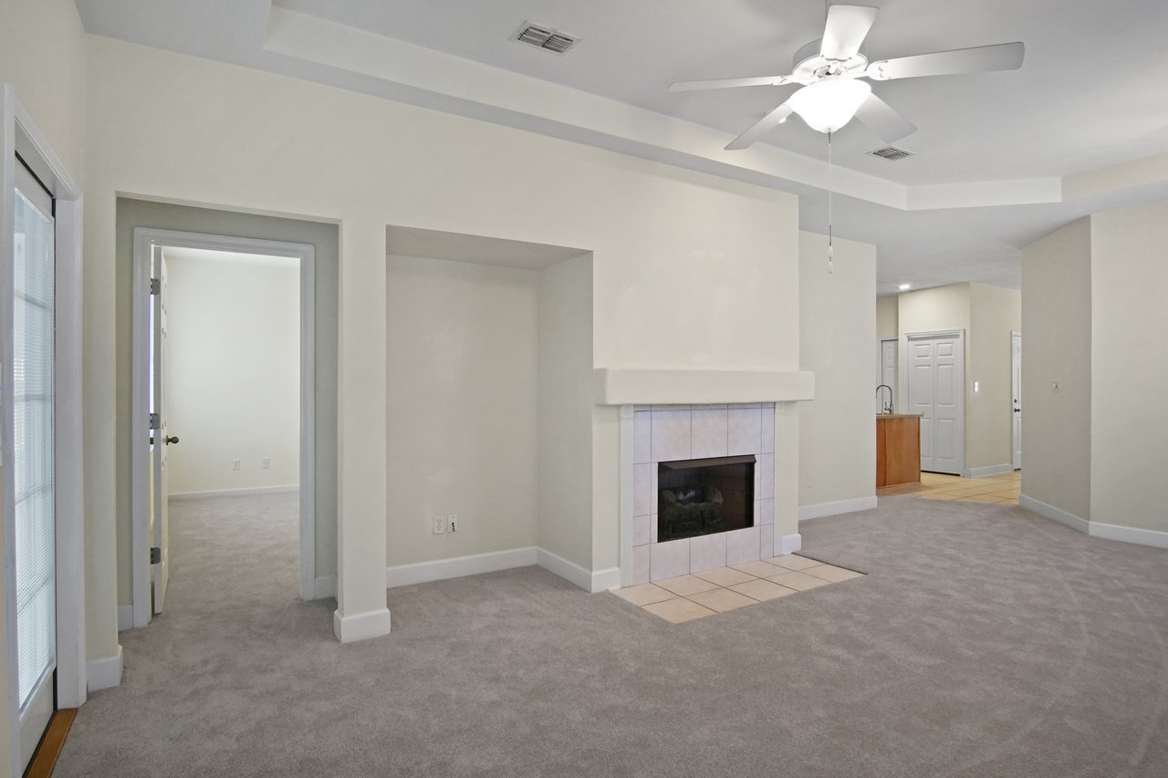 Living room at 5441 Hampton Hill Circle, Tallahassee, Florida 32311 featuring tiled fireplace, tray ceiling, and access to bedroom and kitchen.