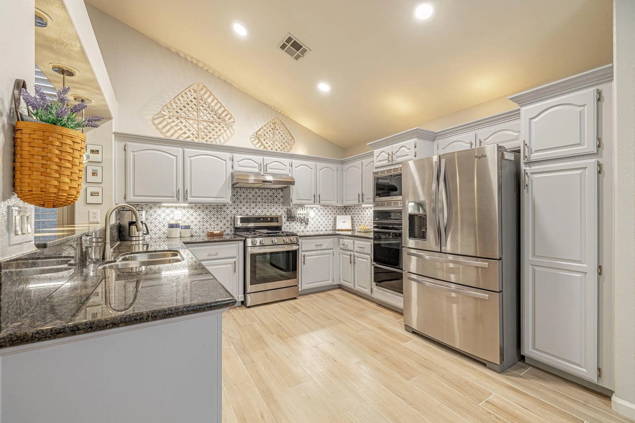 Kitchen with white cabinets, granite counters, patterned backsplash, and stainless steel appliances.