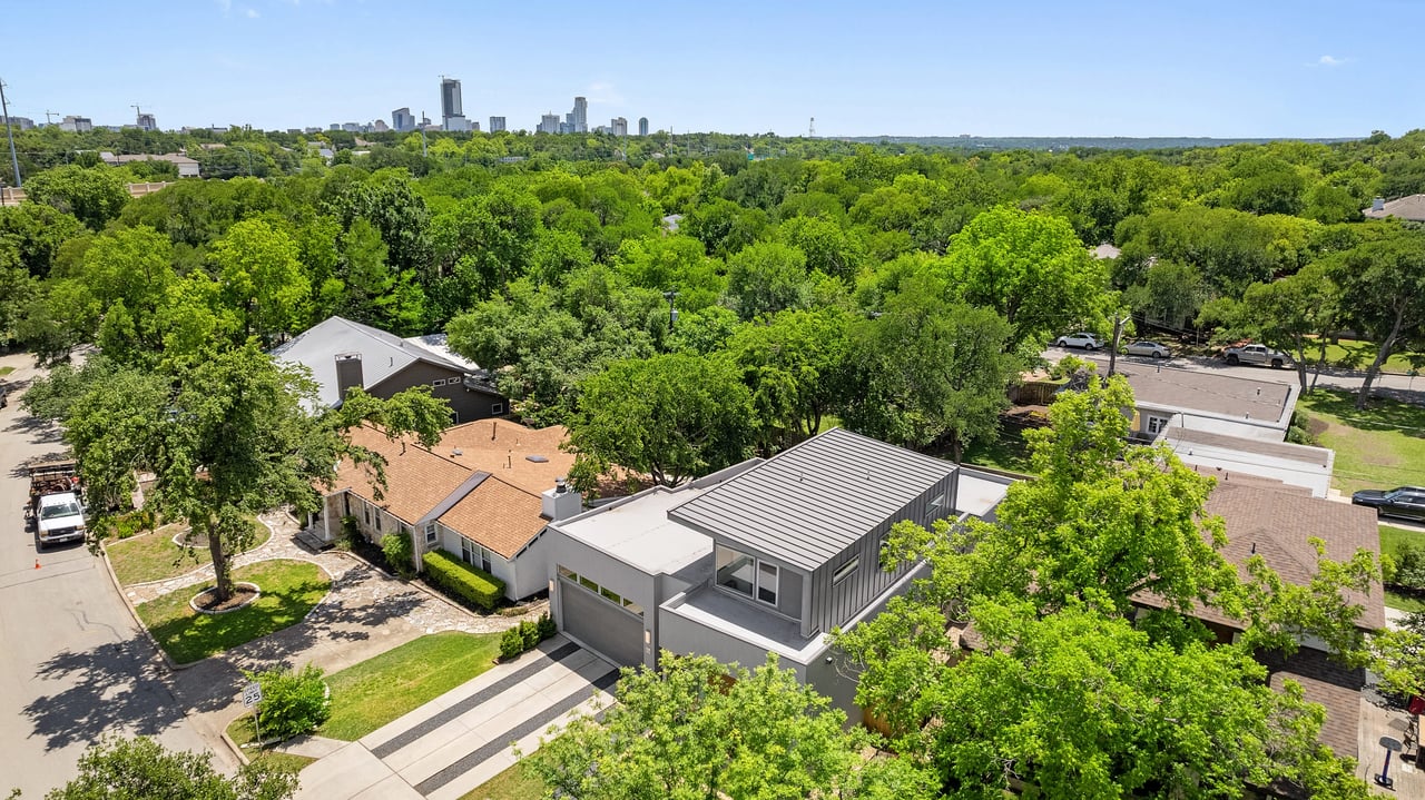 Aerial view over the tree-canopied Tarrytown neighborhood near 34 Margranita Crescent, Austin, TX, with the downtown Austin skyline visible in the distance.