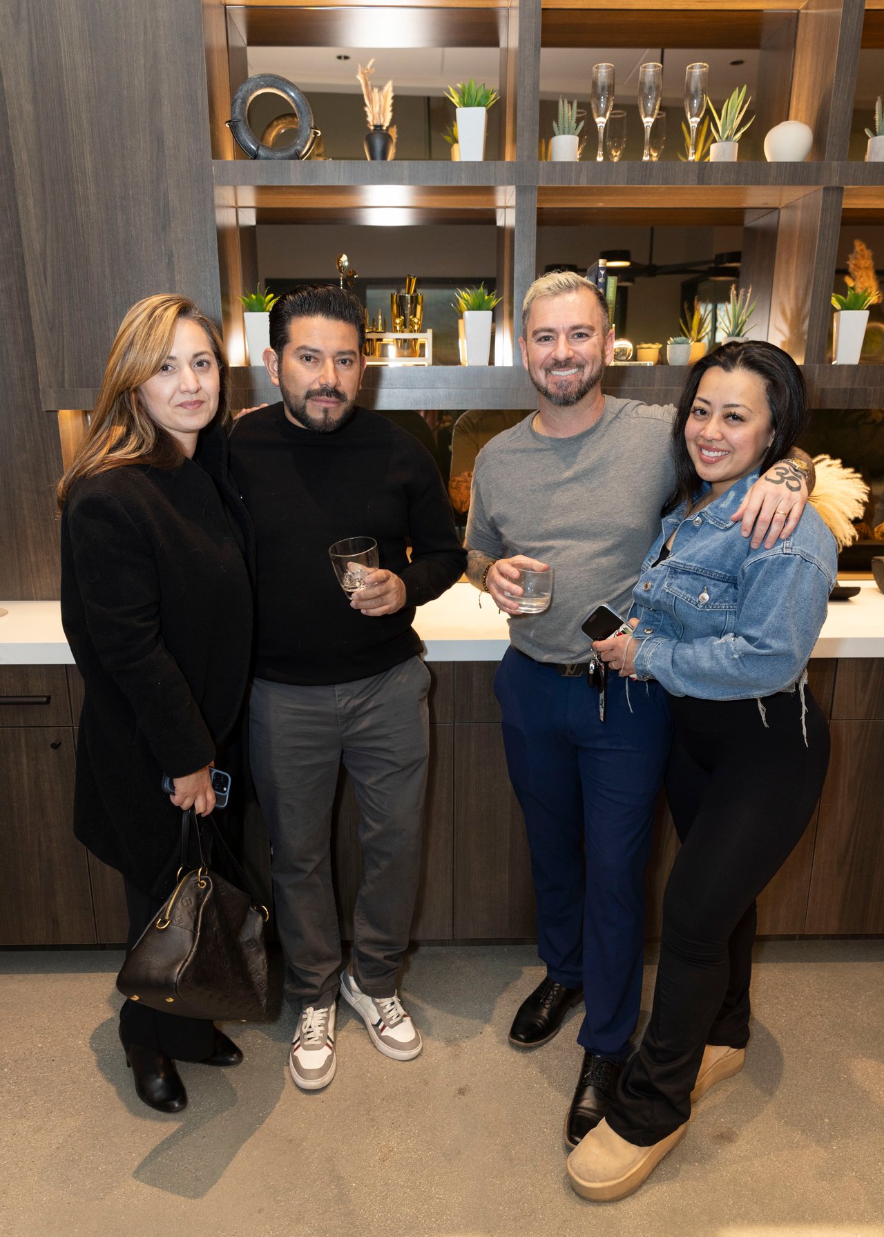 Four adults pose together by display shelves, with two holding glasses.