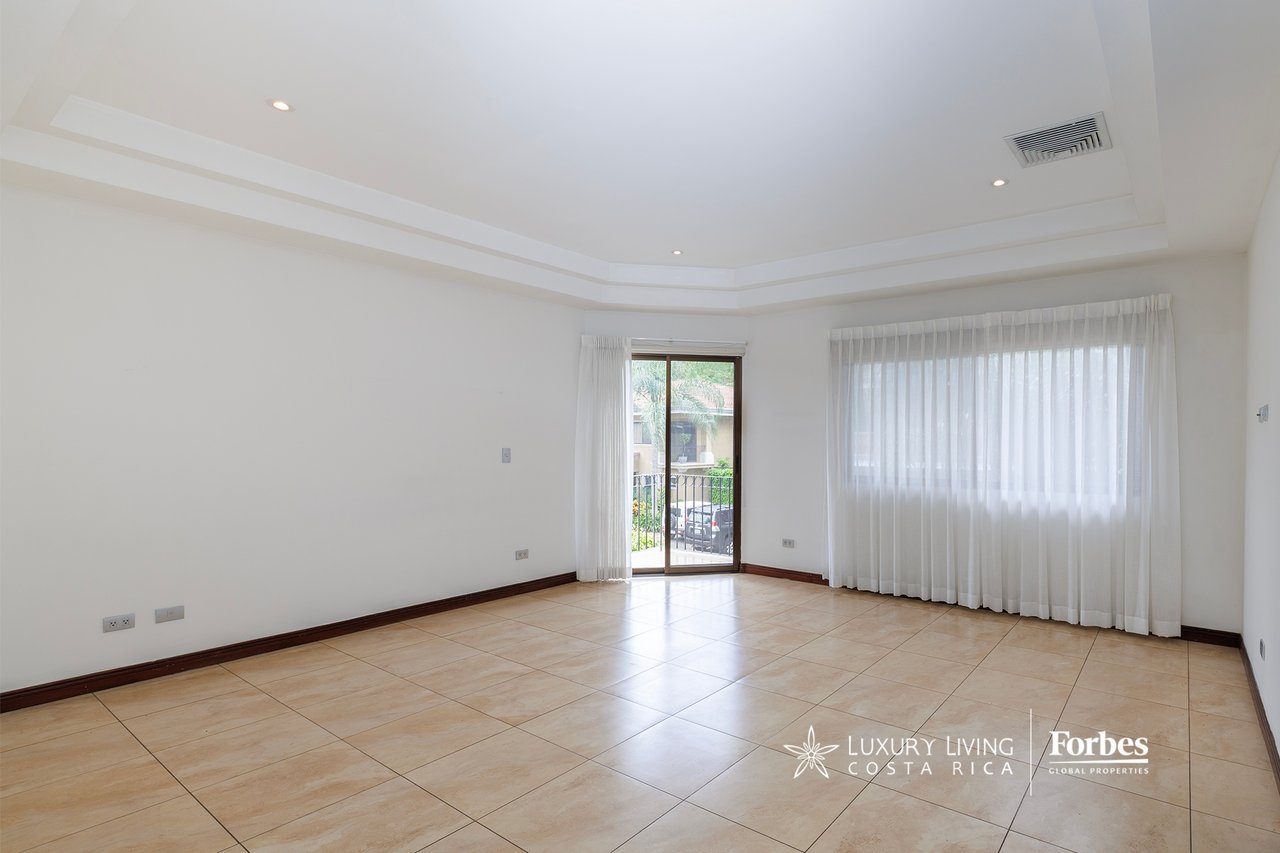 Empty tiled room with white curtains, a wide window, and a sliding glass door to a balcony.