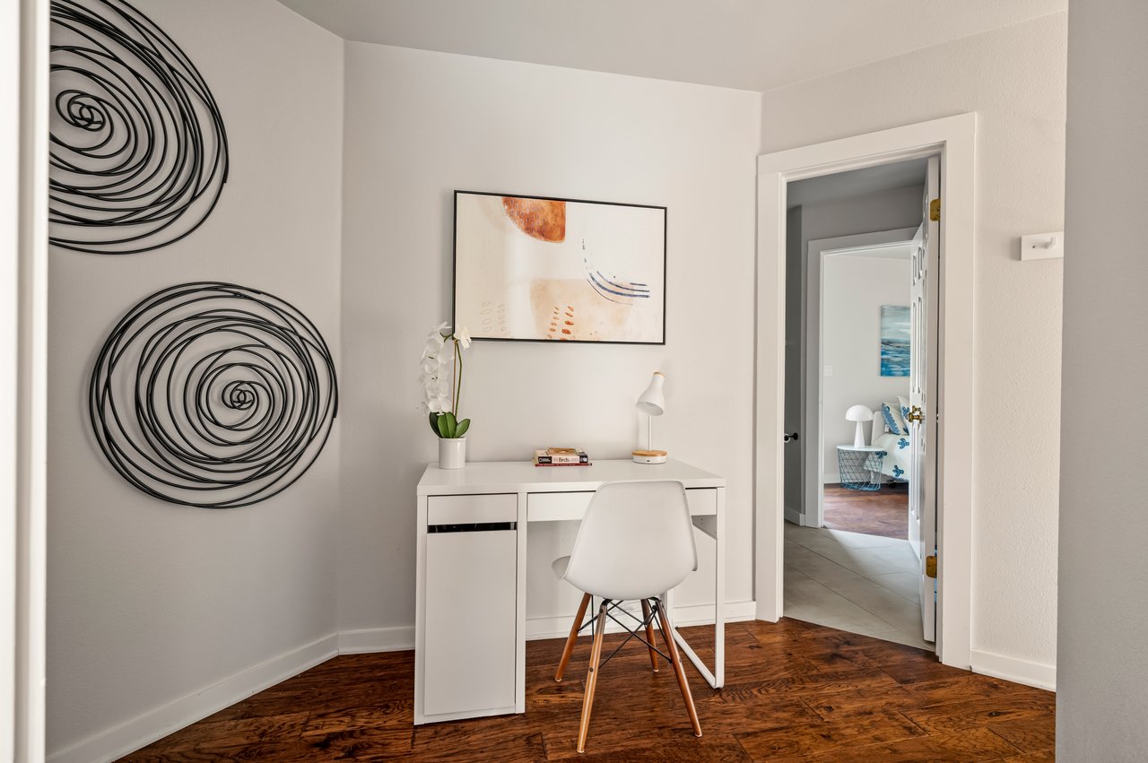 Home office nook with a white desk and chair, spiral wall art, and an open doorway to a bedroom.