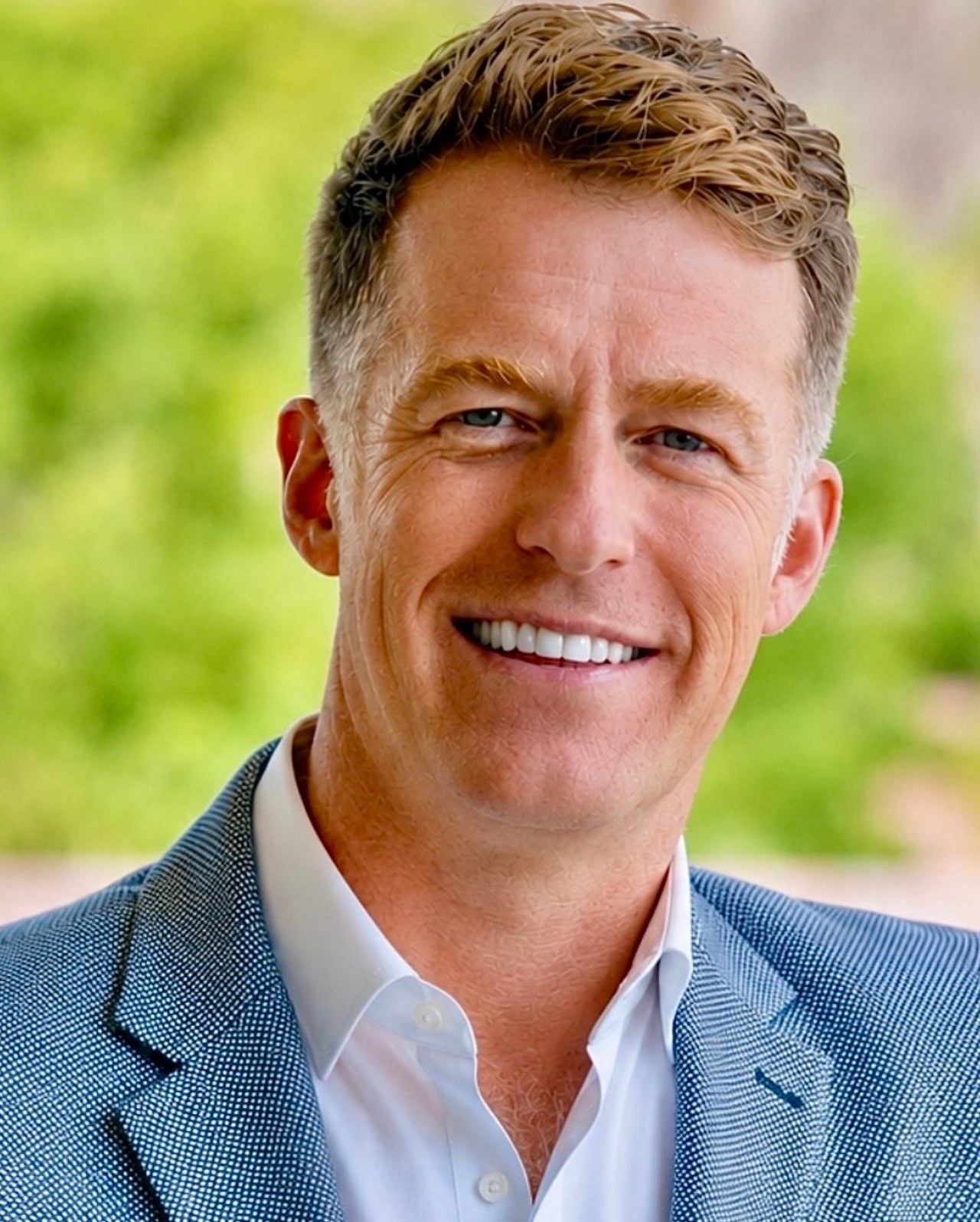 Robert Andrew Millar smiling in a blue patterned blazer against a soft green background.