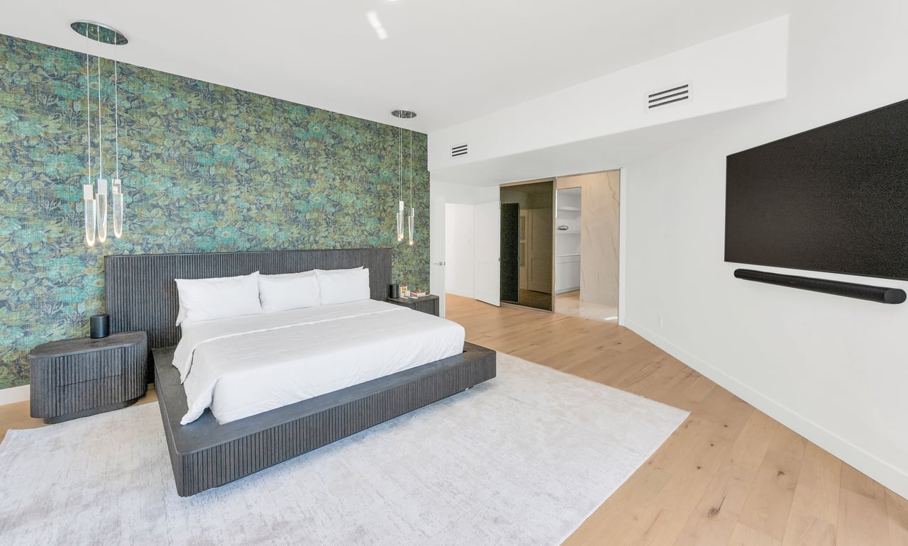 Modern bedroom with a low dark bed, blue-green patterned wall, and light wood floors.
