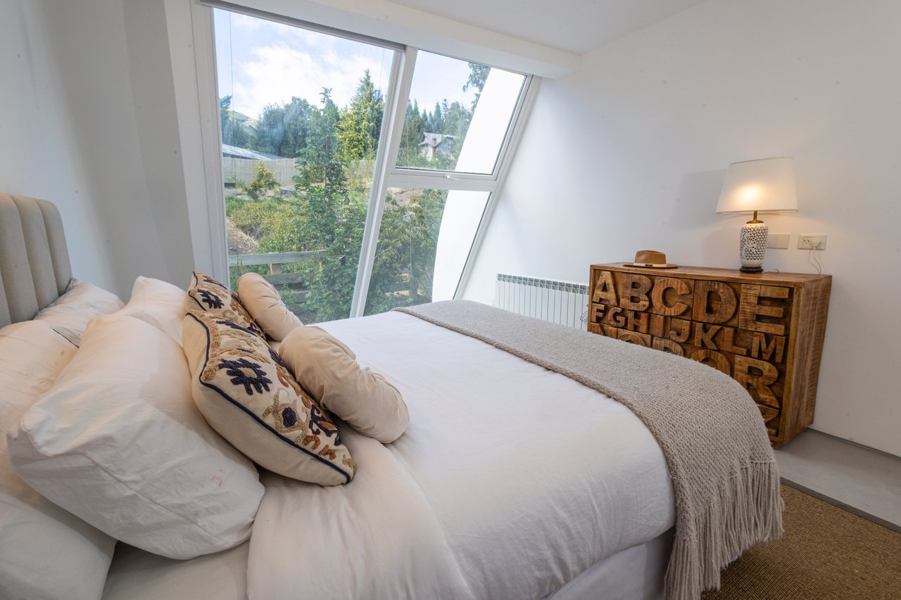 Furnished bedroom with a white bed, slanted windows, and a wooden cabinet carved with alphabet letters.