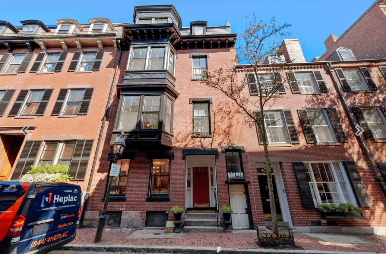 Red-brick townhouse with a prominent dark bay window, black shutters, and a red front door.