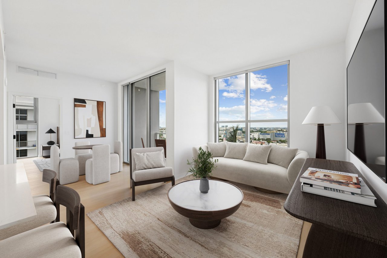 Furnished apartment living room with a curved cream sofa and city views through large windows.