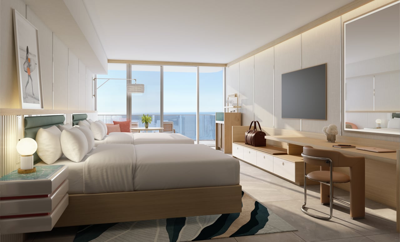 Staged hotel bedroom with two beds, a desk, and ocean views through floor-to-ceiling windows.