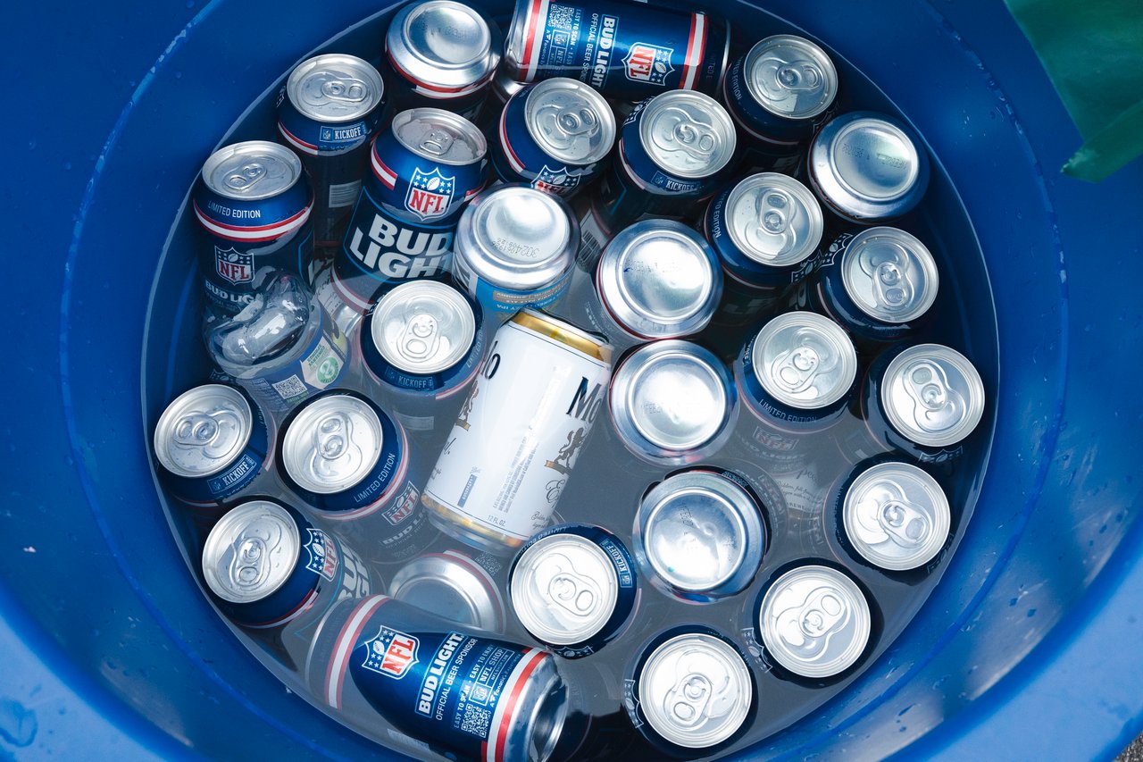 Beer cans packed in ice inside a blue cooler, including Bud Light NFL-themed cans.