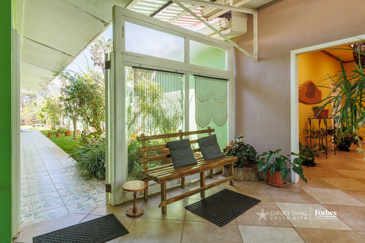 Tiled entryway with a wooden bench and screened doors opening onto a garden walkway.