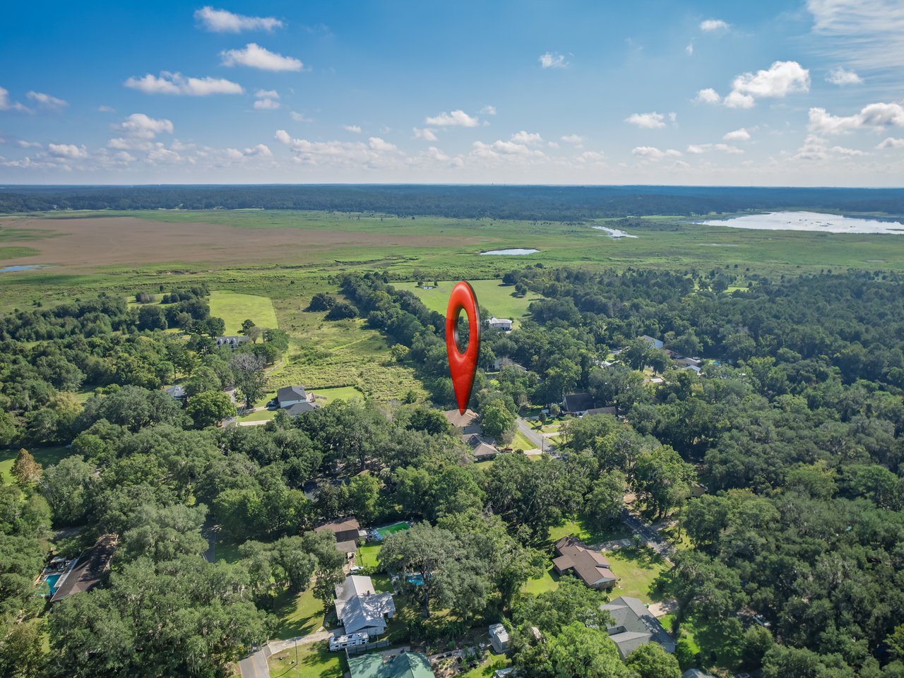 Aerial view of a marked home among trees, with wetlands and water beyond the neighborhood.