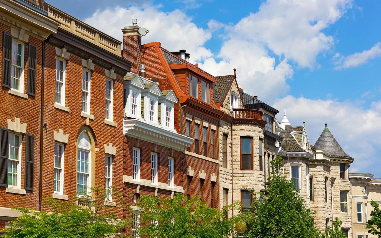 Historic rowhouses with varied brick and stone facades rise above leafy trees.