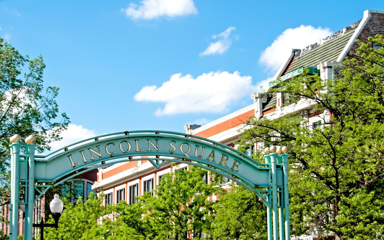Lincoln Square neighborhood sign framed by leafy trees and nearby buildings.