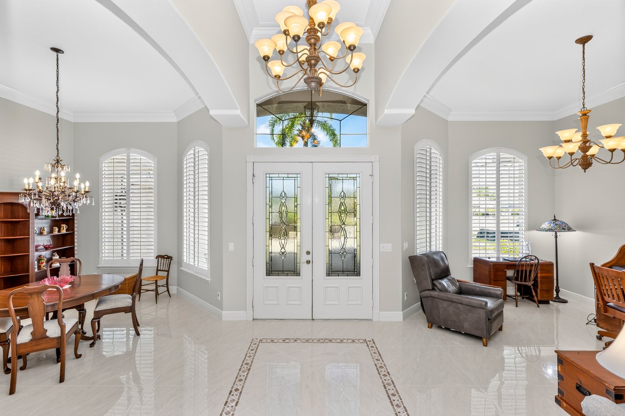 Furnished foyer with a high arched ceiling, ornate chandeliers, marble flooring, and decorative-glass double doors.