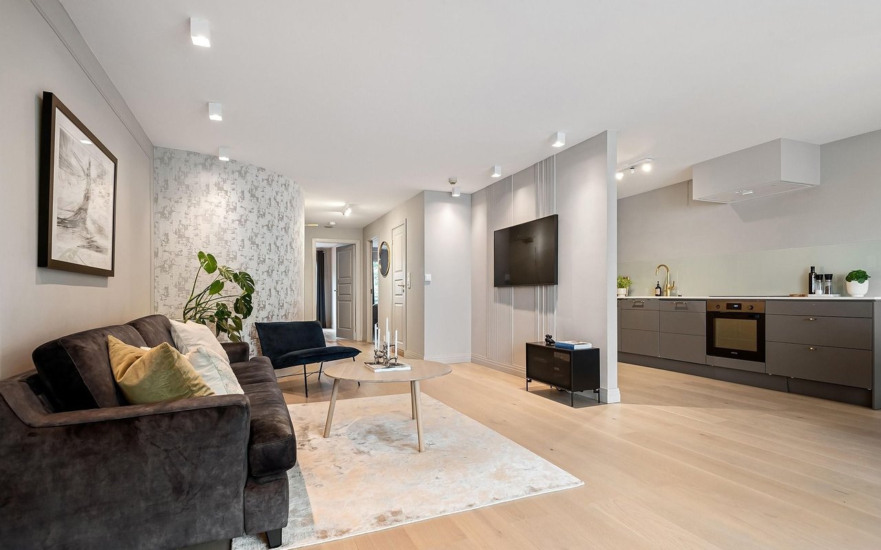 Open-plan living room and kitchen with a dark sofa, pale wood floors, and gray cabinetry.
