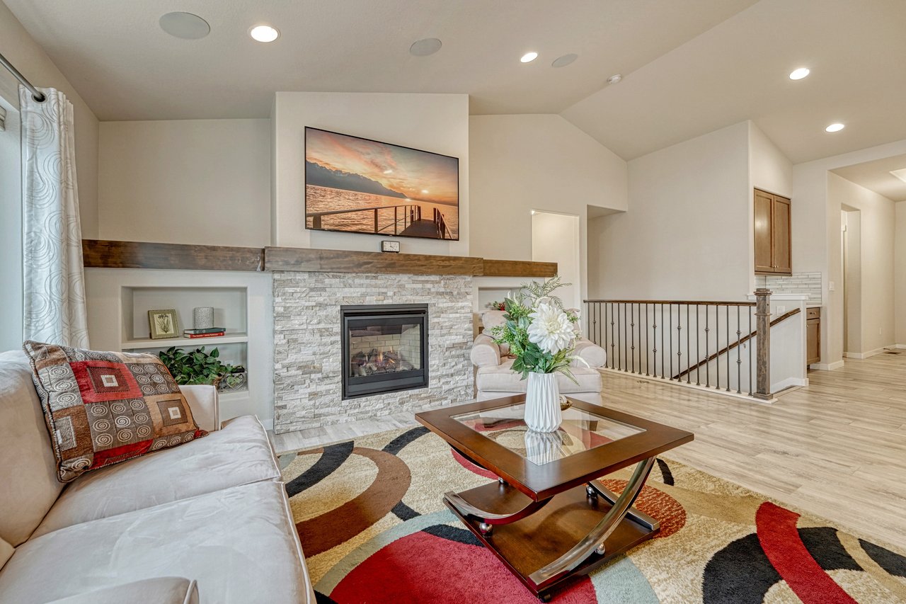 Living room with stacked-stone gas fireplace, wood mantel and built-in shelves beside the stair railing