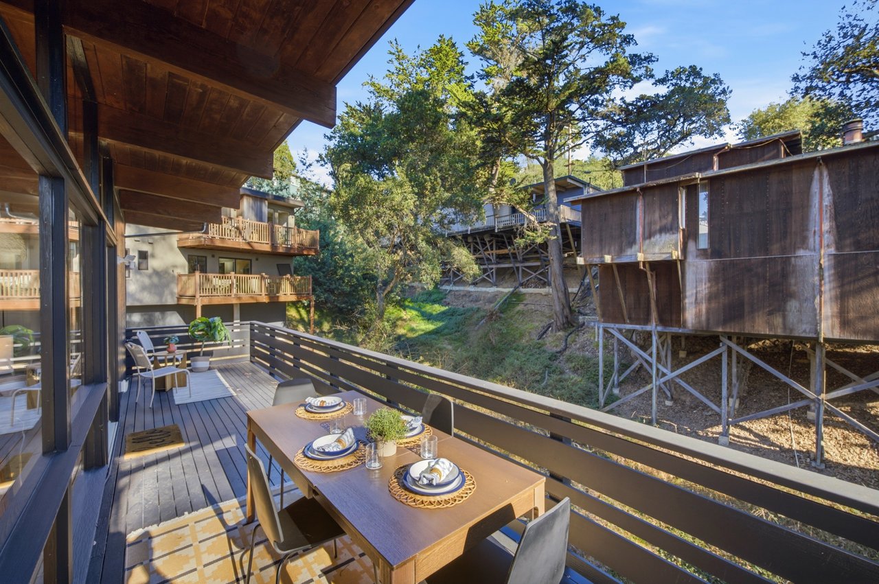 Wooden deck dining area overlooking a wooded hillside, with outdoor table and chairs.