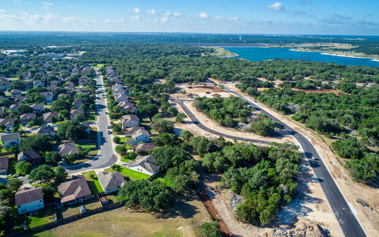 Aerial neighborhood beside a reservoir, with a bridge and new subdivision roads under construction.