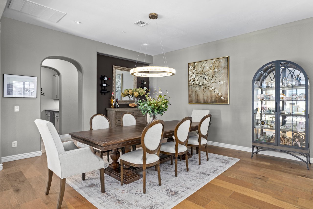 Formal dining room with a wooden table, upholstered chairs, chandelier, artwork, and a glass display cabinet.