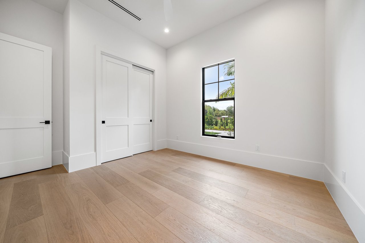 Empty room with light wood floors, a sliding closet door, and a black-framed window.