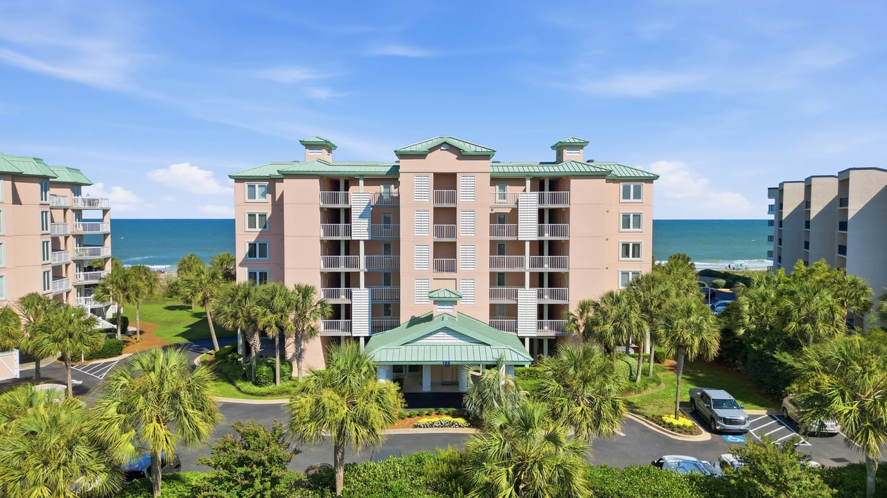 Oceanfront condominium with green roofs, balconies, and palm-lined grounds.