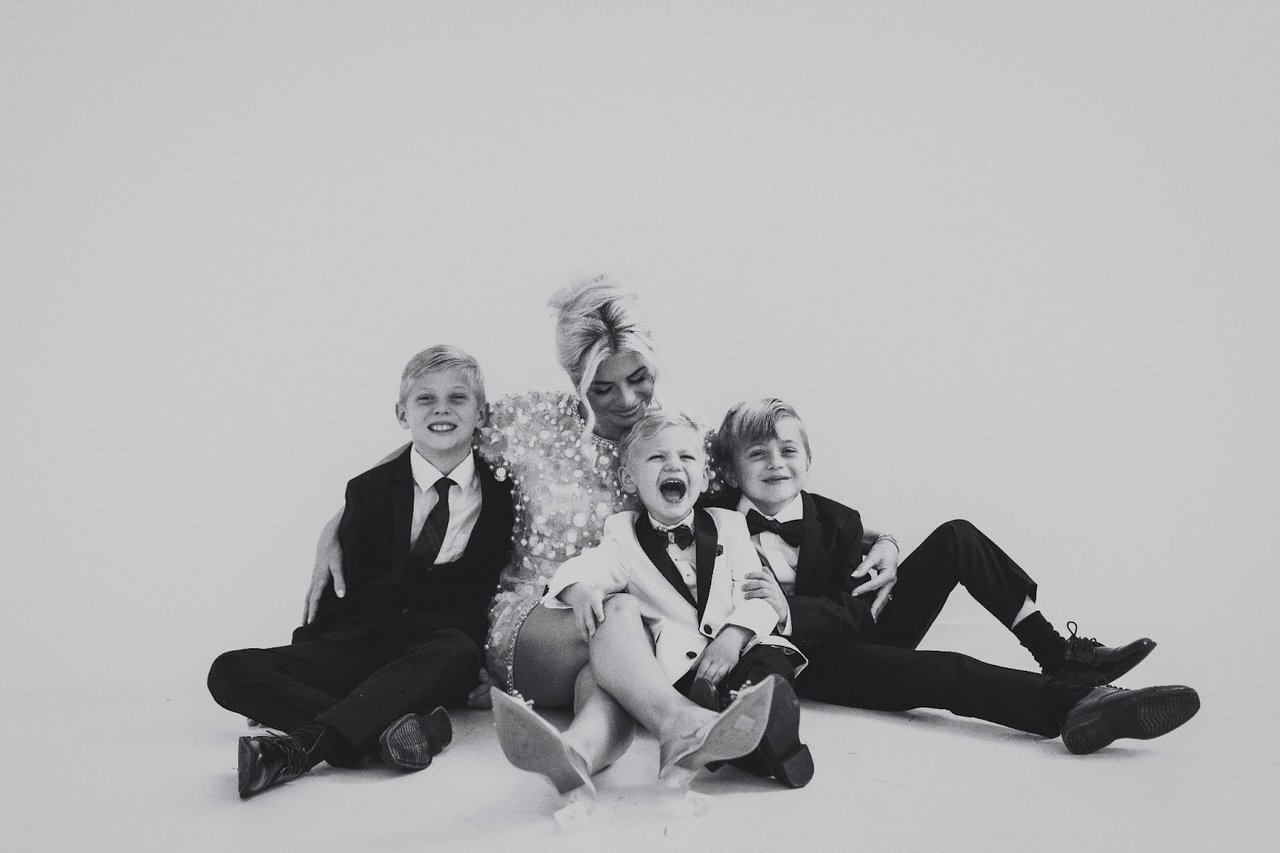 A woman sits with three boys in formal clothes in a black-and-white family portrait.