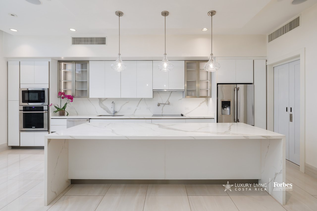 Modern white kitchen with a large marble-patterned waterfall island and three glass pendant lights.