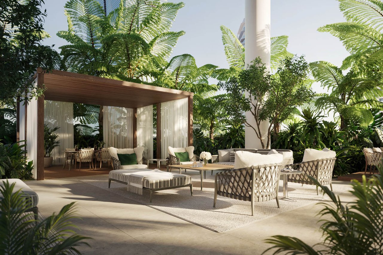 Outdoor lounge with woven seating beneath a wooden pergola, surrounded by tropical greenery.
