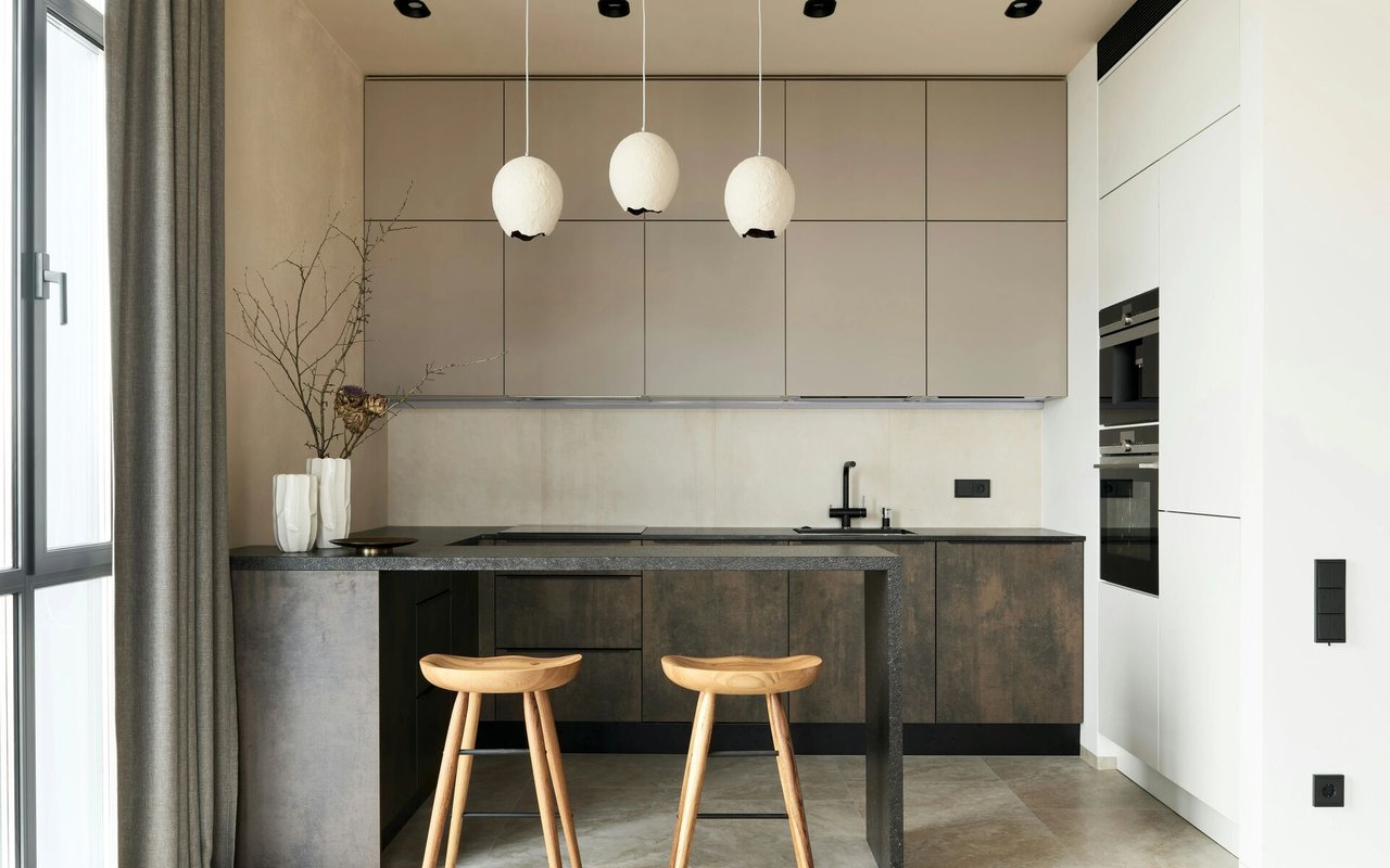 Modern kitchen with dark stone counters, two wooden stools, and three pendant lights.