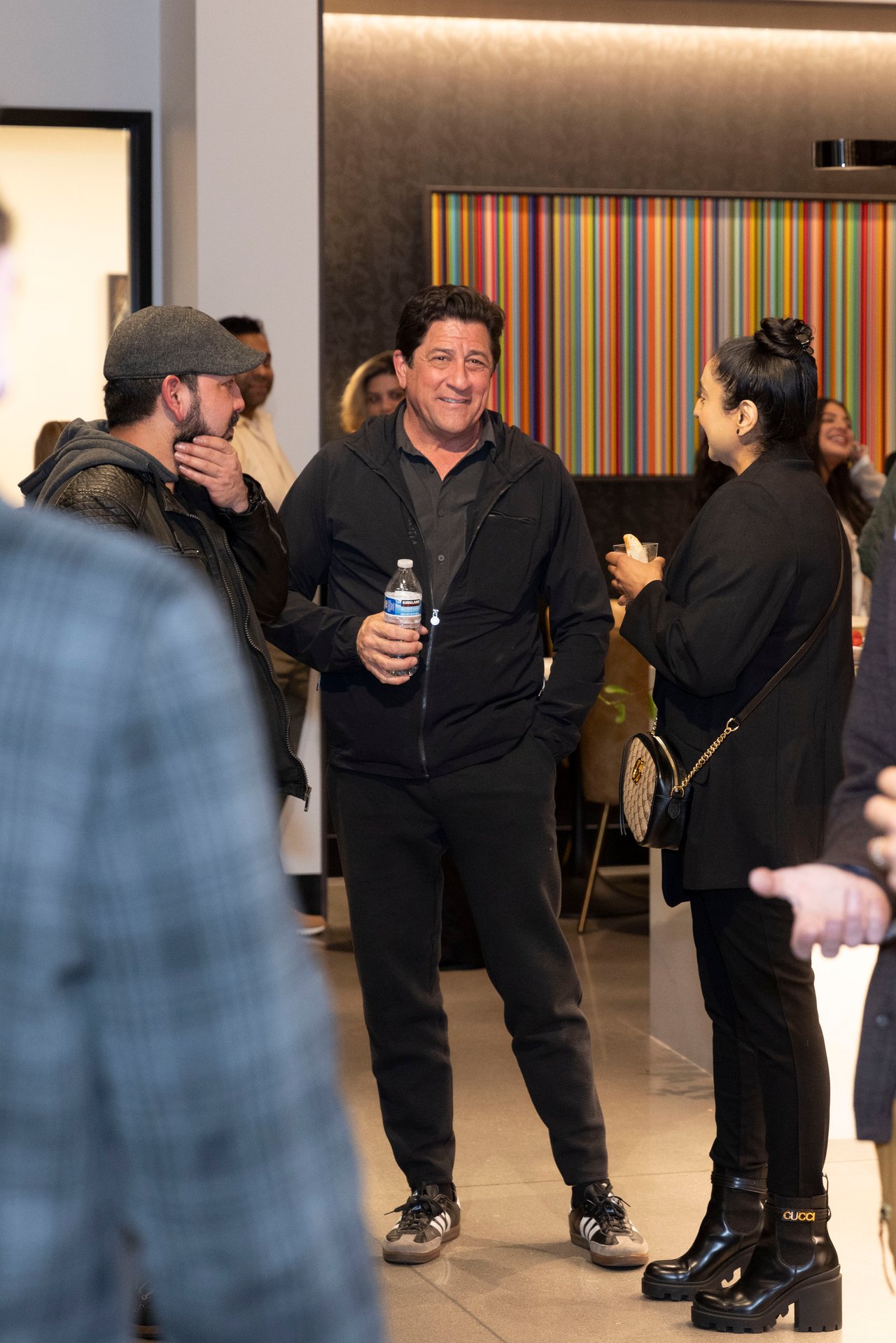 Guests chat at an indoor gathering in front of a colorful striped wall panel.
