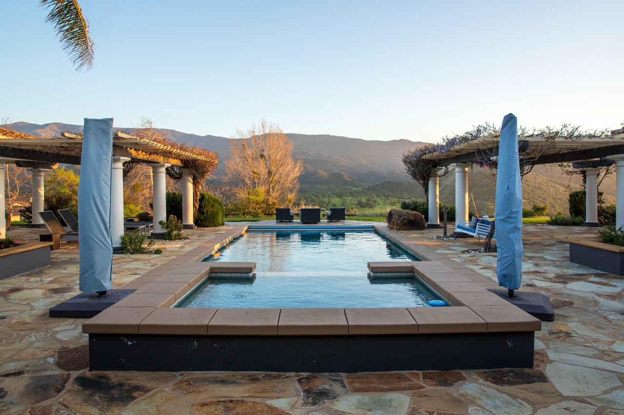 Swimming pool framed by pergolas, with a mountain view beyond the patio.