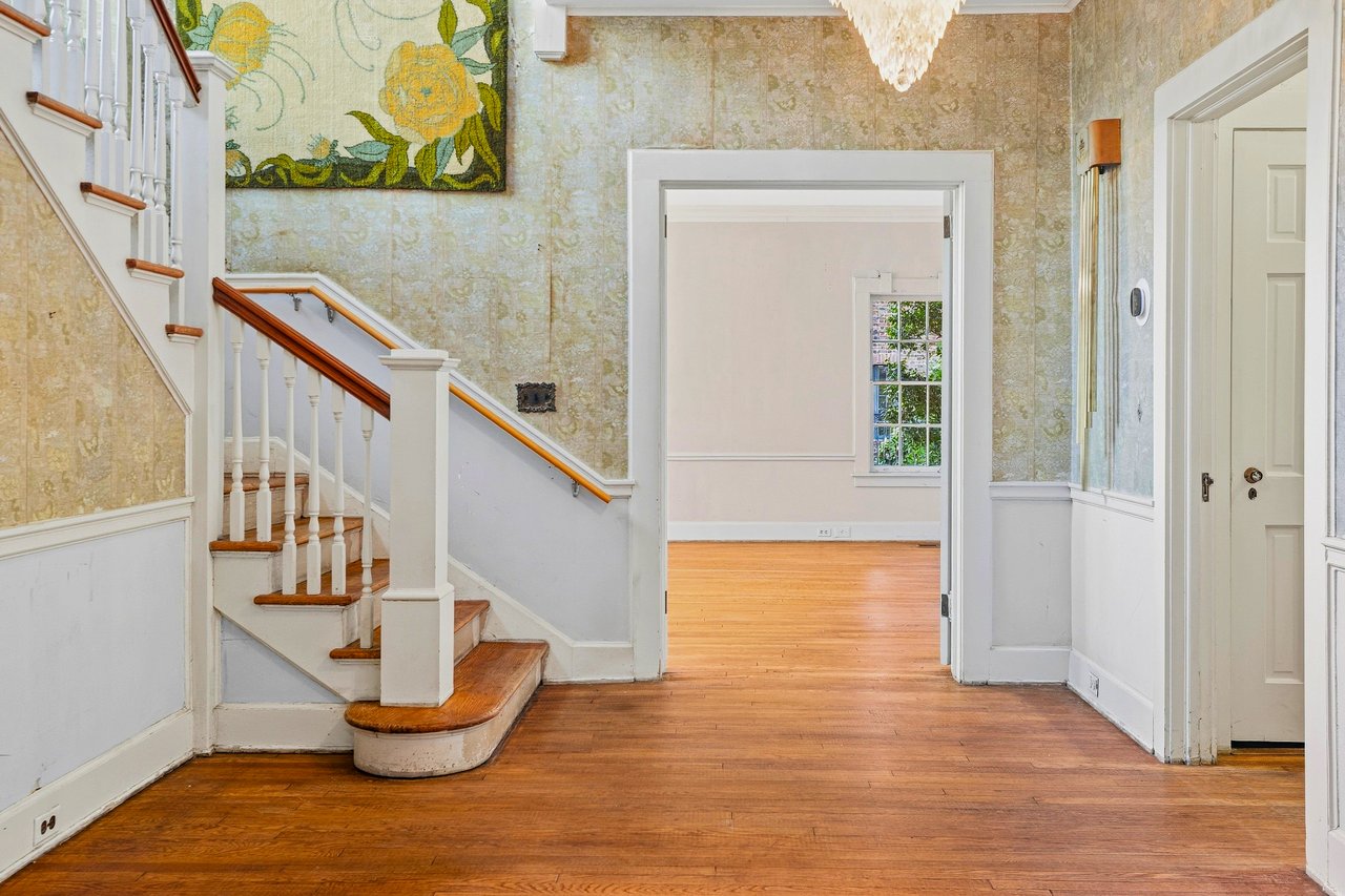 Entry hall with a white staircase, patterned gold wallpaper, and polished hardwood floors.