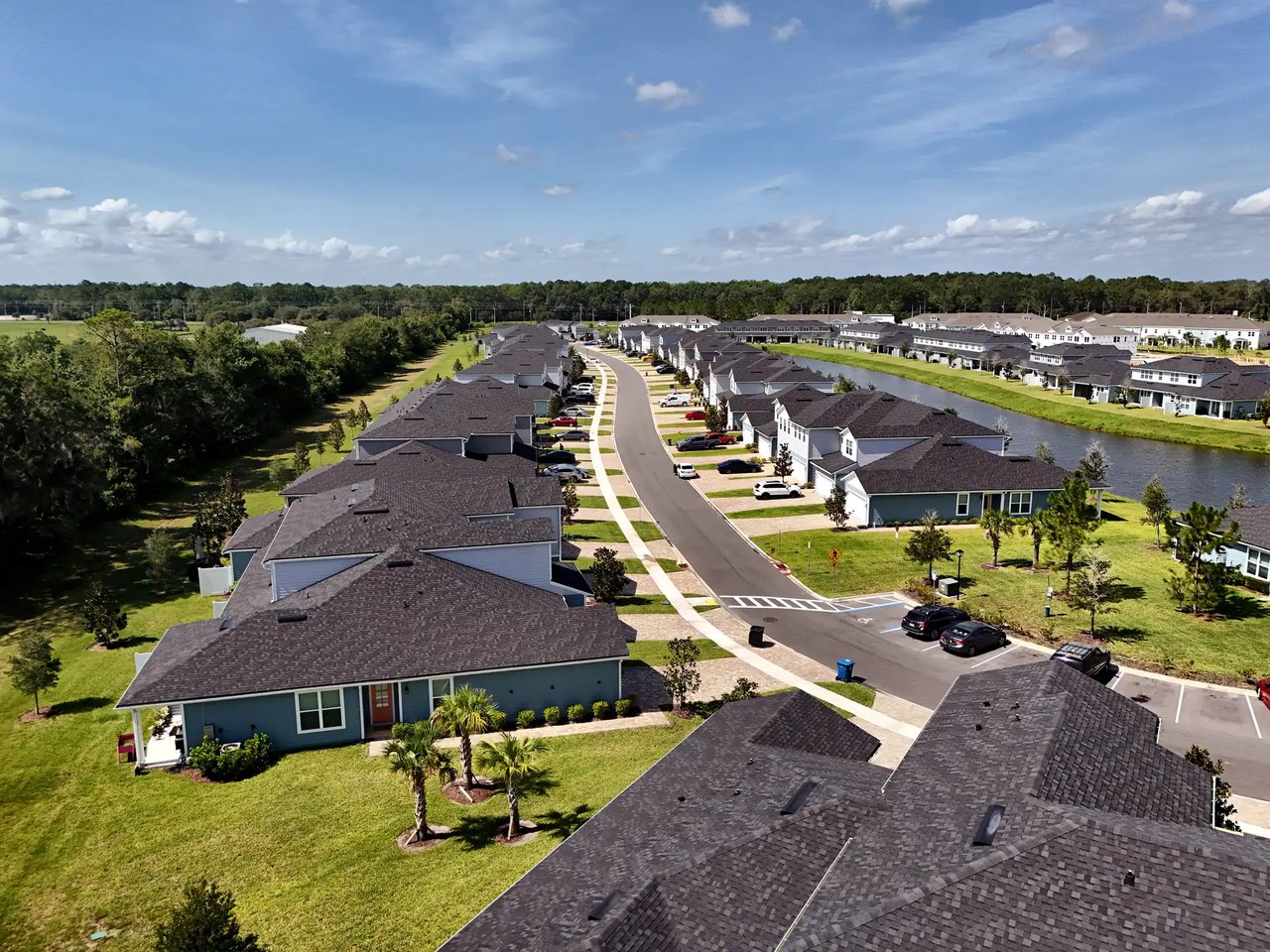 Aerial view of homes along a neighborhood street beside a pond and green space.