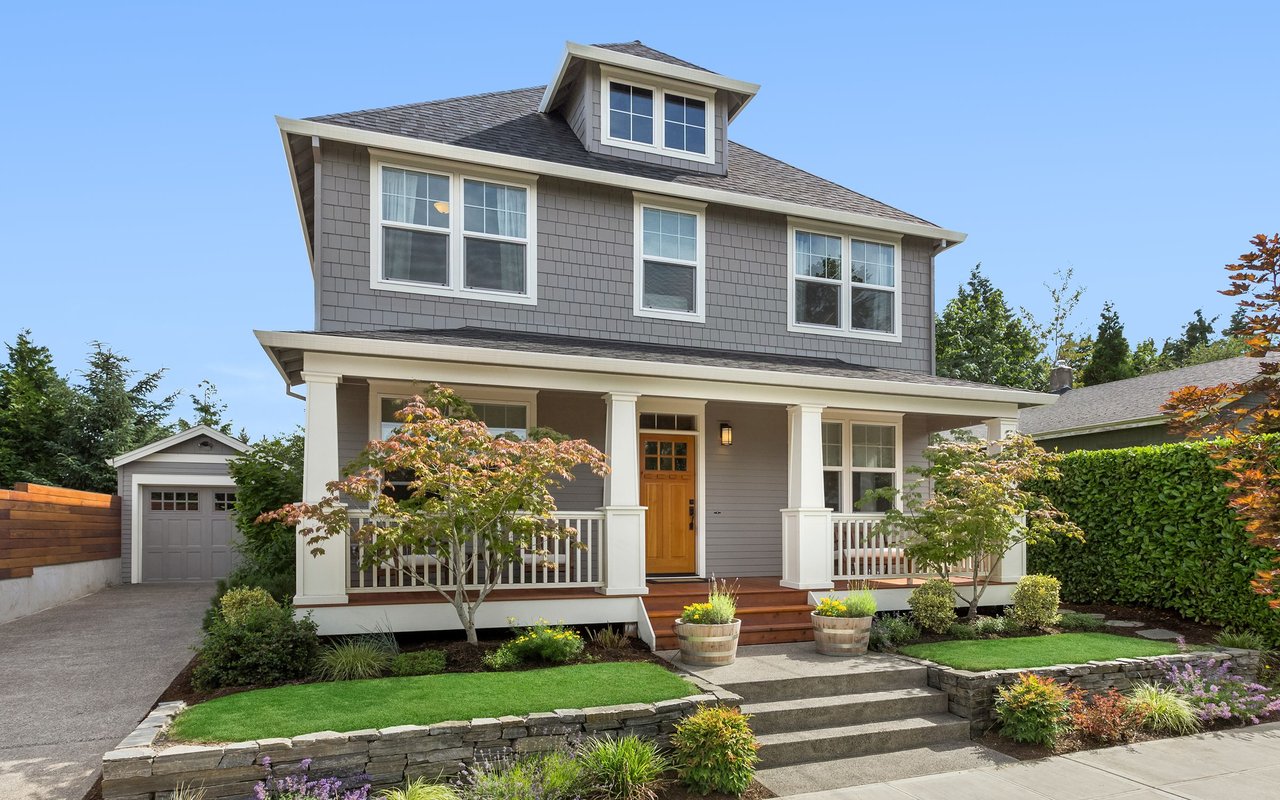 Gray two-story house with a white-columned porch, wooden front door, and landscaped yard.
