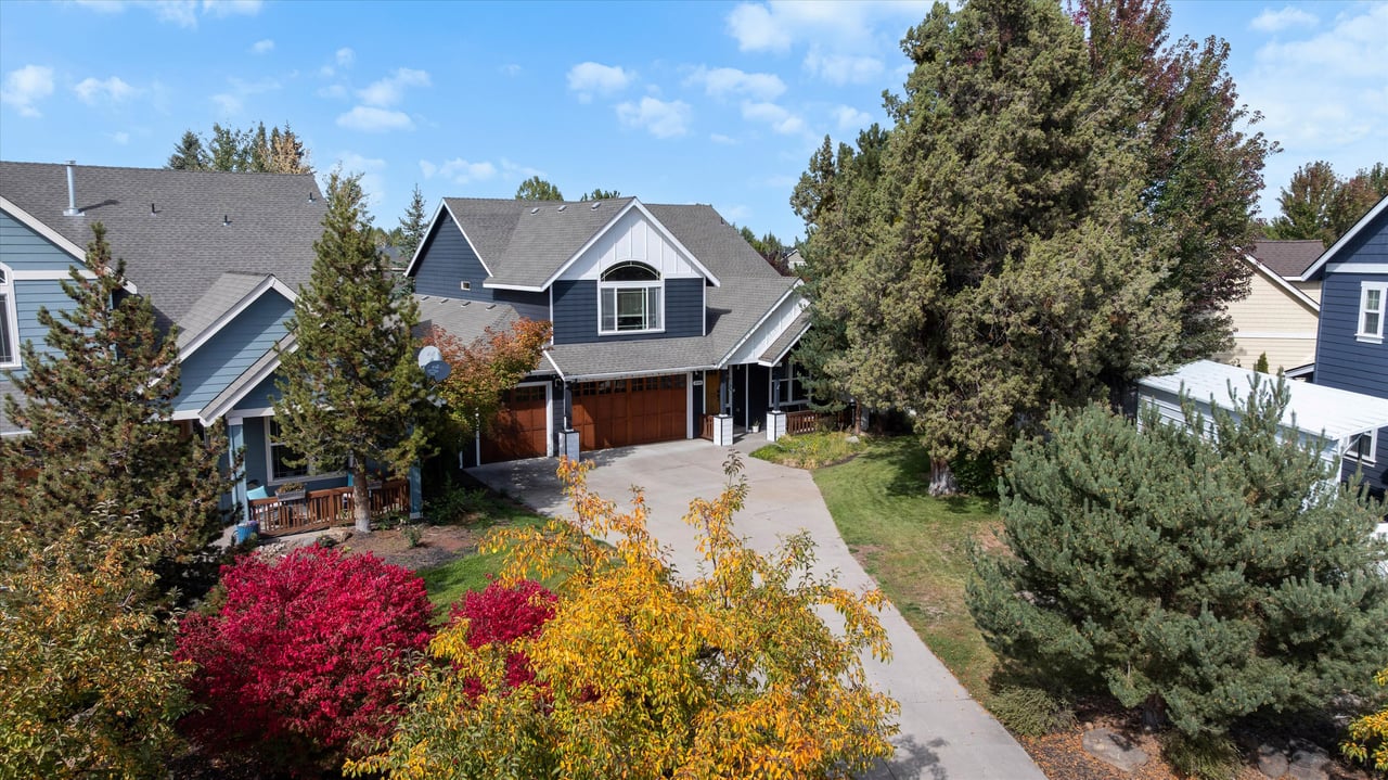 Blue-gray two-story home with wooden garage doors, a broad driveway, and colorful autumn landscaping.